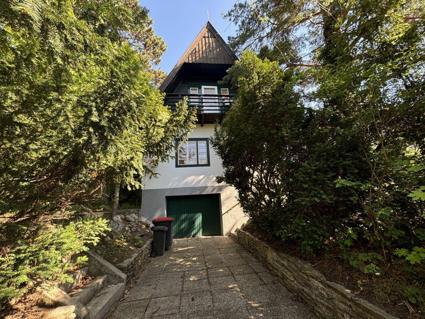 Vorderansicht eines Hauses im Chalet-Stil mit Garage und umgeben von hohen Bäumen.