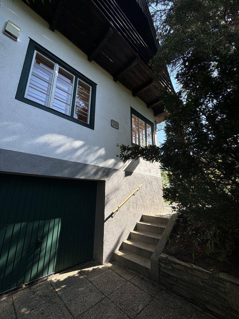 Seitenansicht des Hauses mit Garage, Außentreppe und umgeben von Bäumen.
