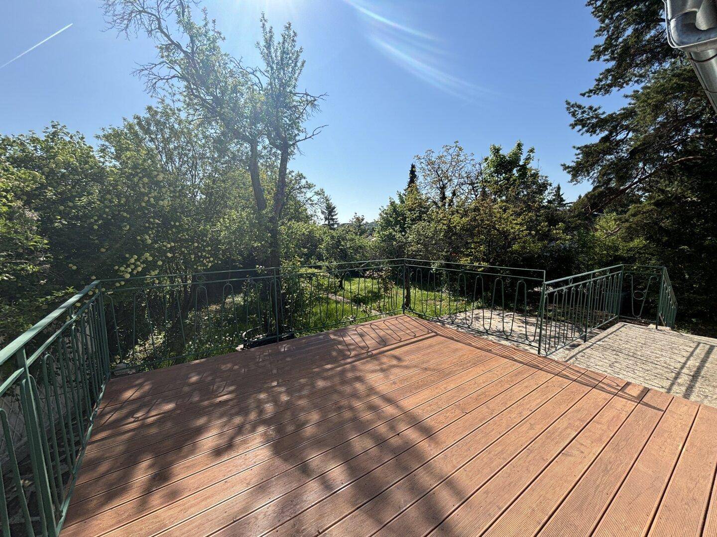 Große Holzterrasse mit Metallgeländer und weitem Blick über die grüne Landschaft.