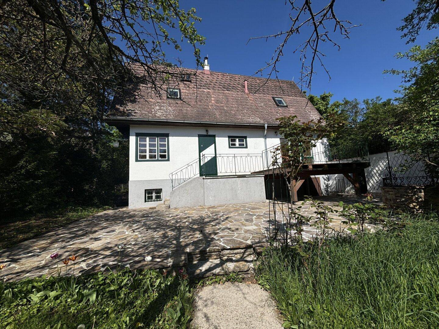 Malerisches Landhaus umgeben von viel Grün, mit Steinterrasse und Dachfenstern.