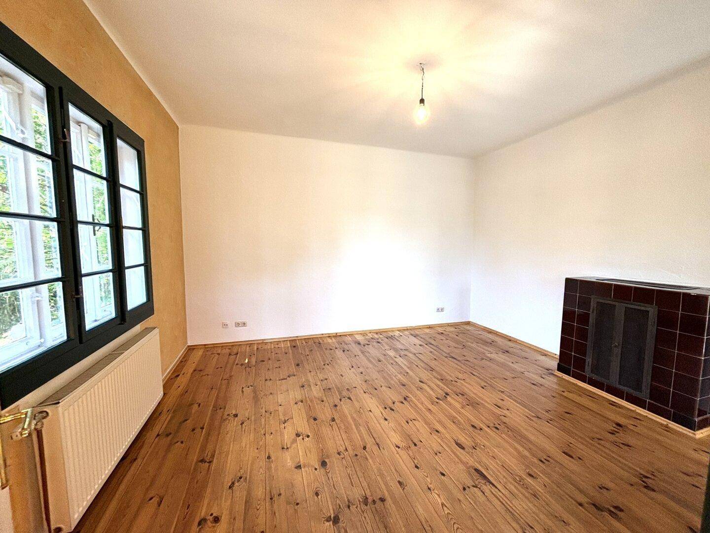Geräumiges Zimmer mit Holzdielenboden, weißer Wand und einem traditionellen Kachelofen.