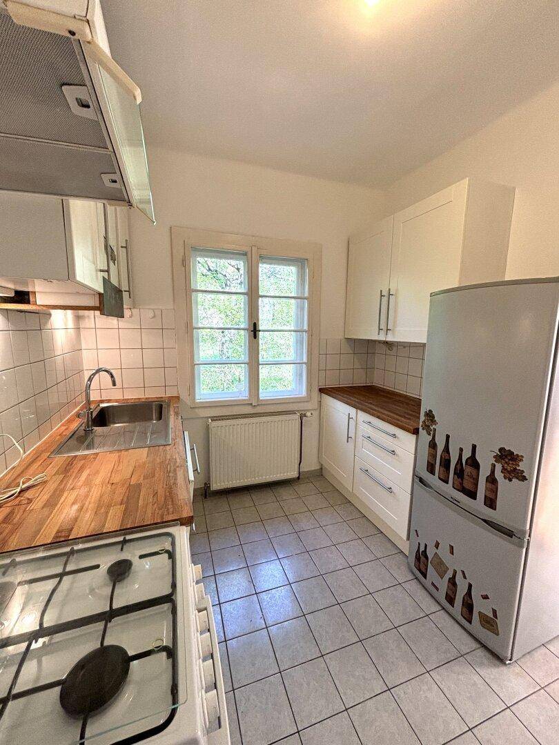Funktionale Küche mit weißen Schränken, Holz-Arbeitsplatte, Fliesenboden und Fenster.