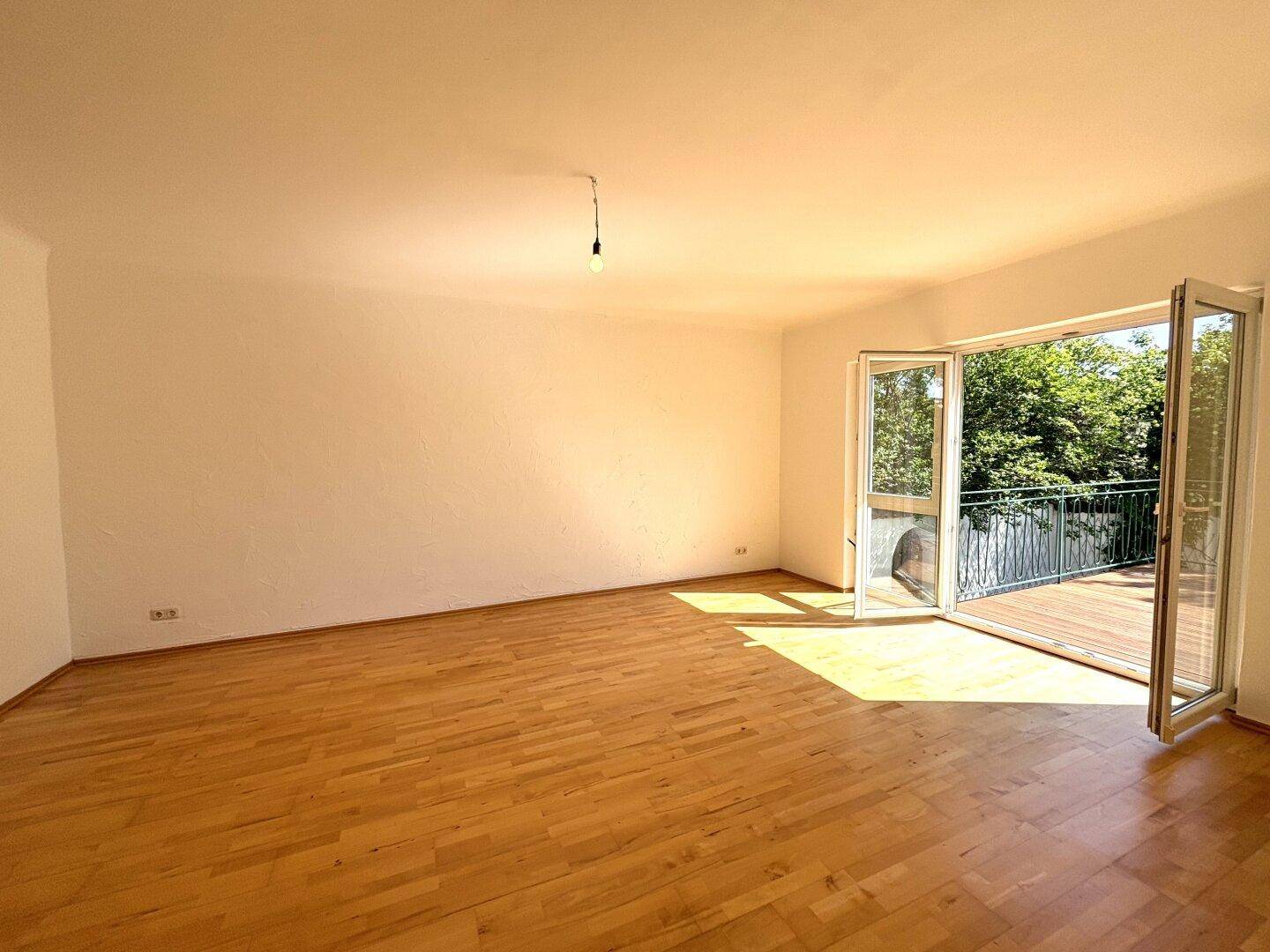 Helles Wohnzimmer mit Parkettboden und großen Fenstertüren, die auf einen Balkon führen.