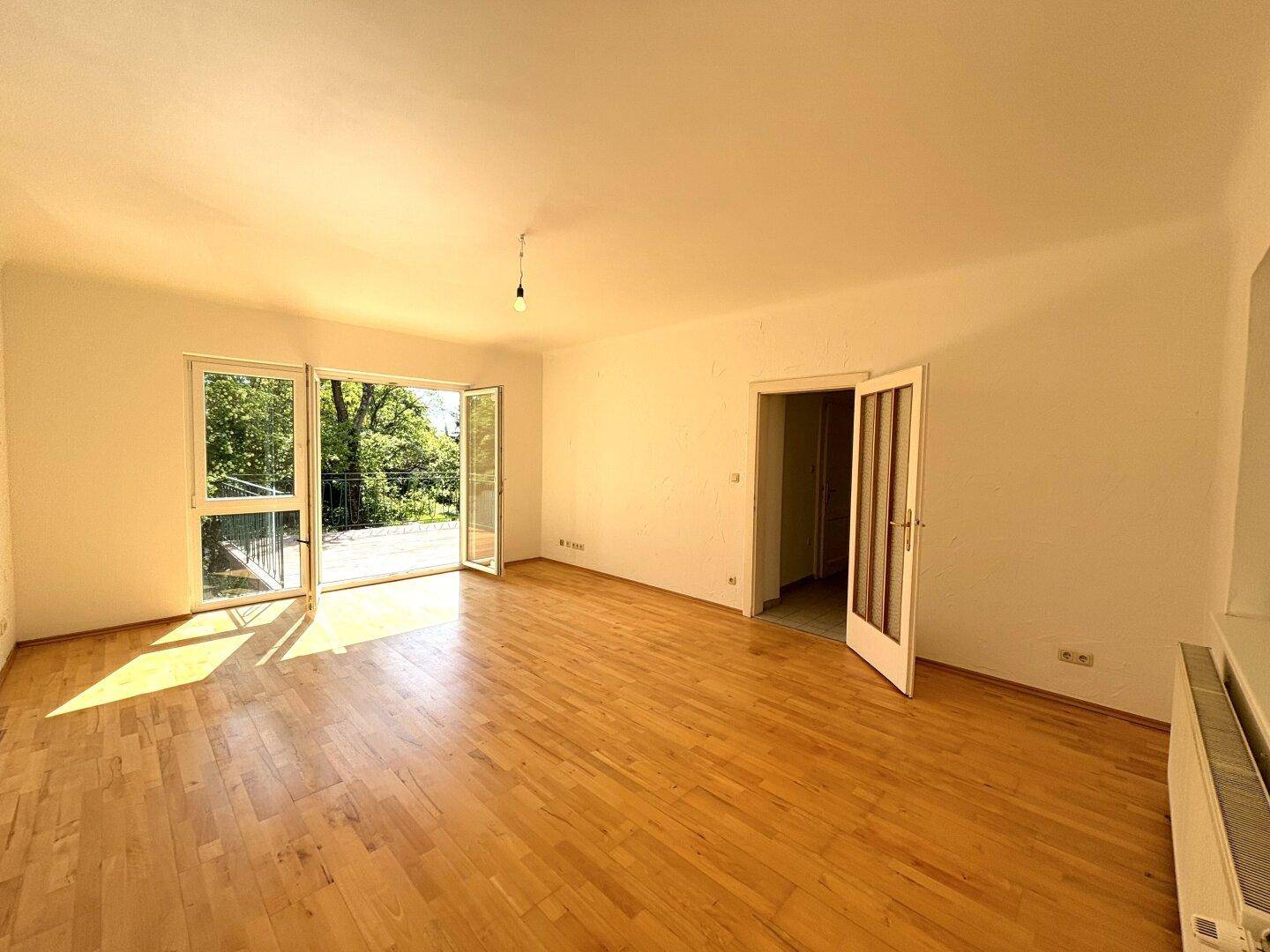 Lichtdurchflutetes Wohnzimmer mit Parkettboden und Zugang zu einem sonnigen Balkon.