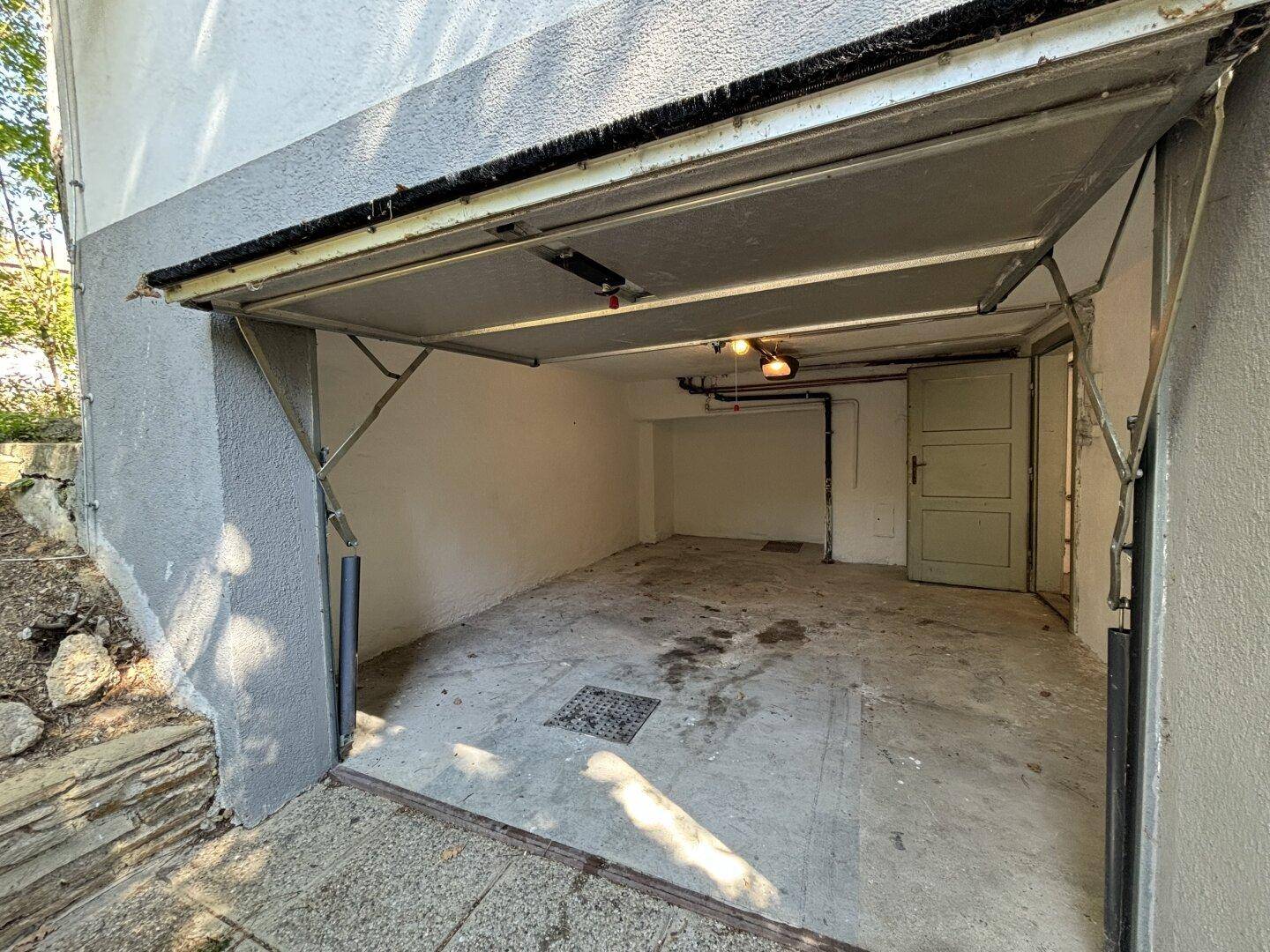 Leere Garage mit geöffnetem Tor und Betonboden, bereit zur Nutzung.