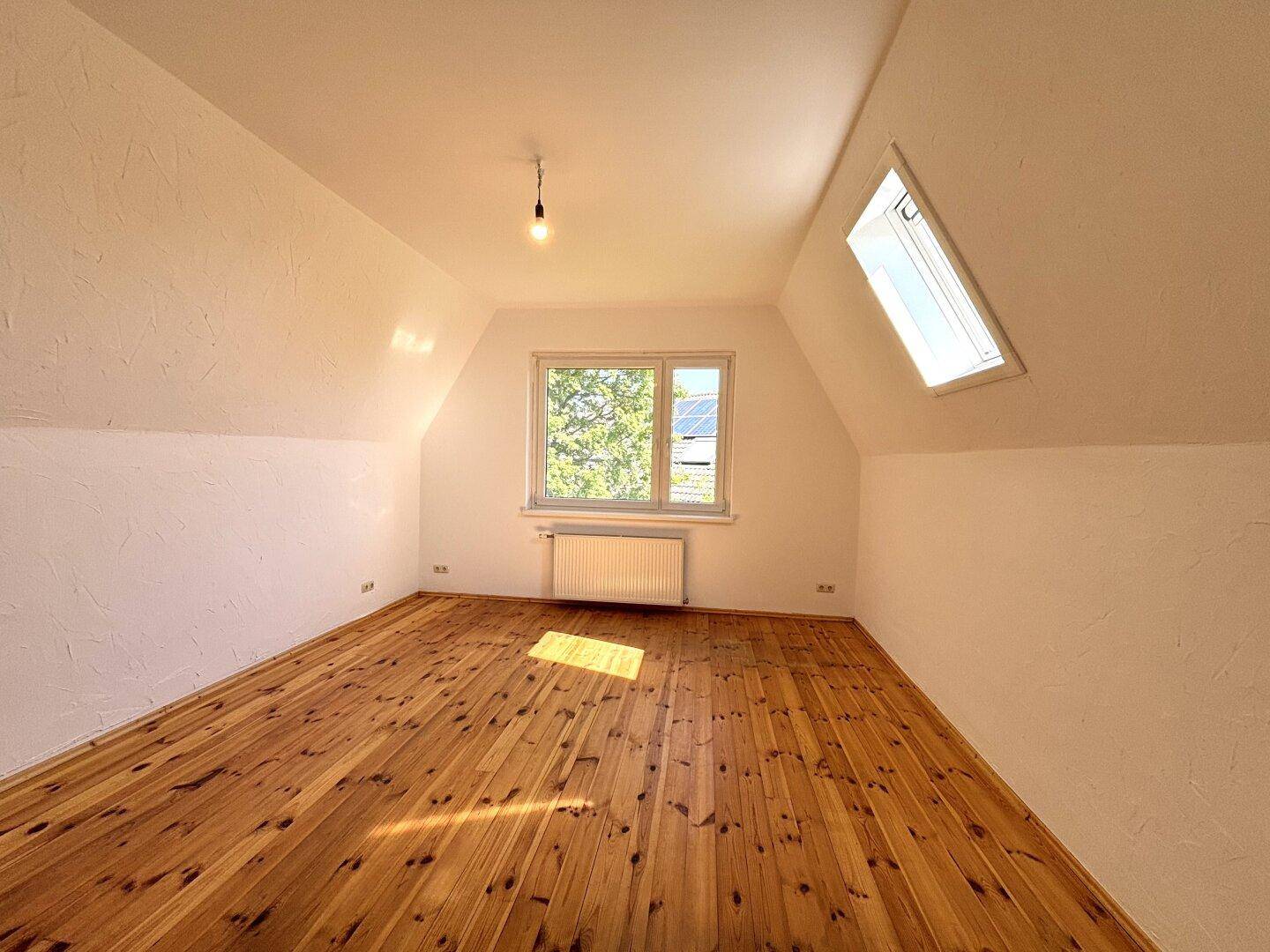 Helles Schlafzimmer im Dachgeschoss mit Holzdielenboden, Dachfenster und Blick ins Grüne.