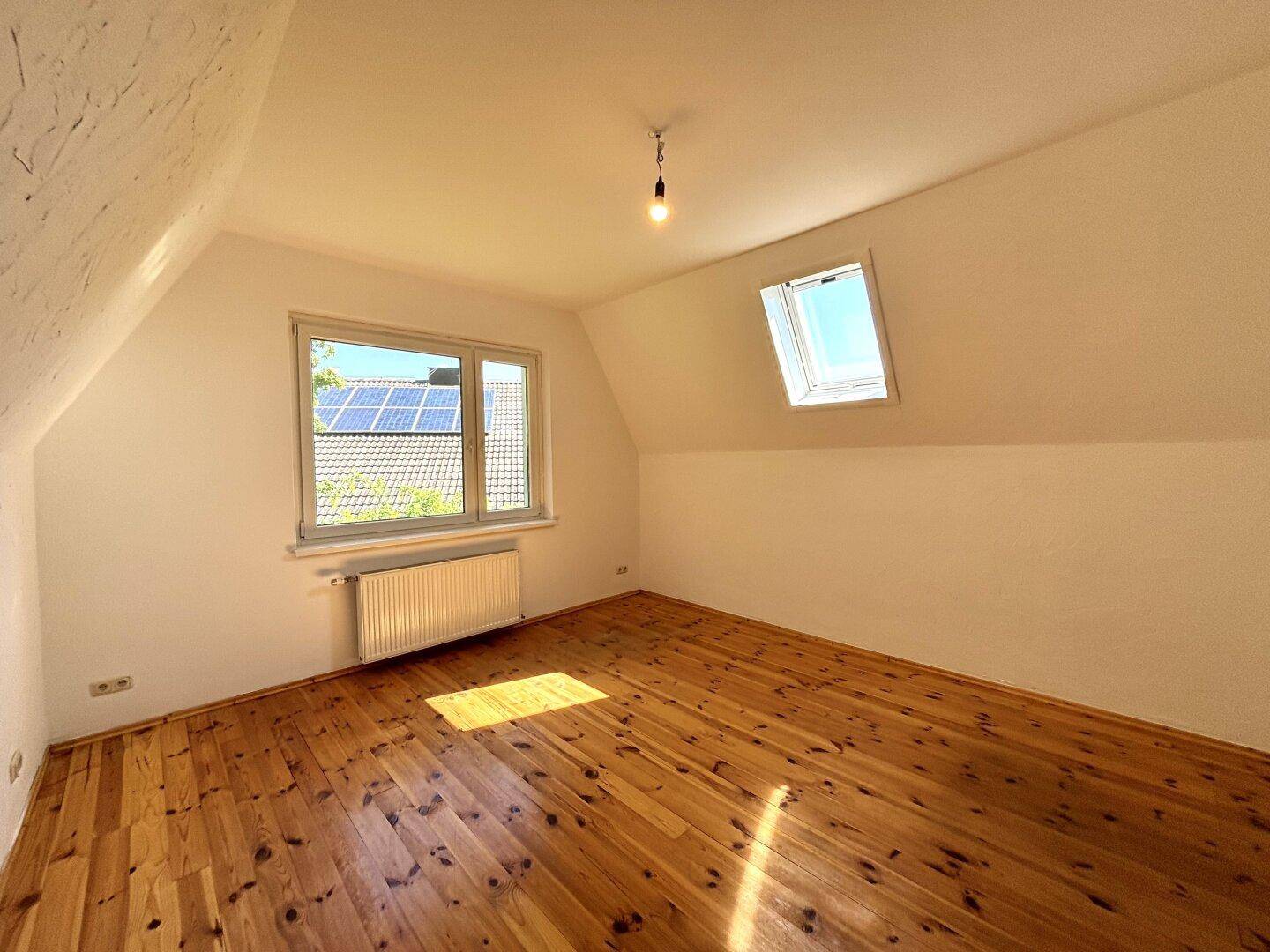Schlafzimmer im Dachgeschoss mit Holzdielenboden, Dachfenster und Blick auf Solaranlagen.