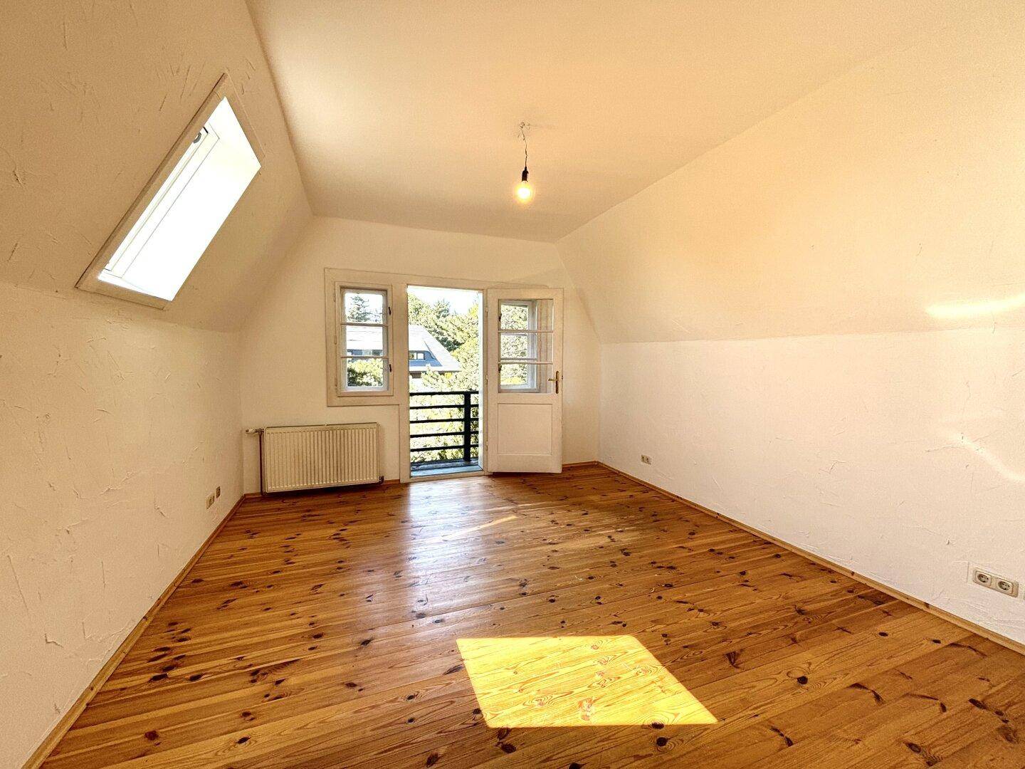 Dachgeschoss-Schlafzimmer mit Holzdielenboden, Dachfenster und Zugang zu einem französischen Balkon.