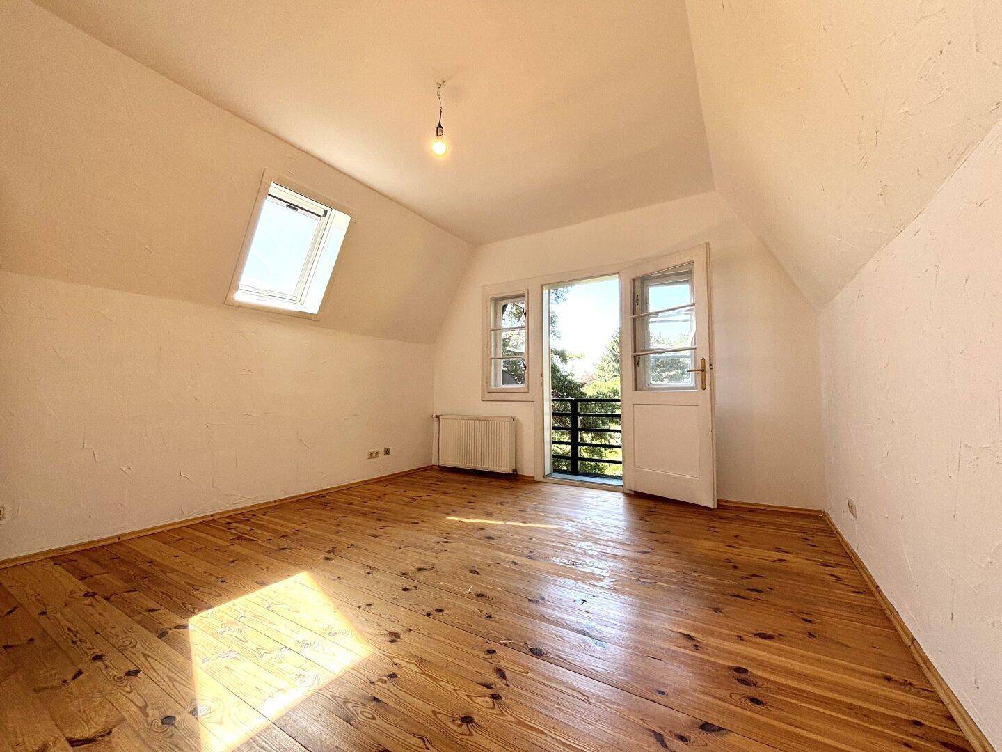 Helles Dachgeschoss-Schlafzimmer mit Holzdielenboden und Zugang zu einem französischen Balkon.