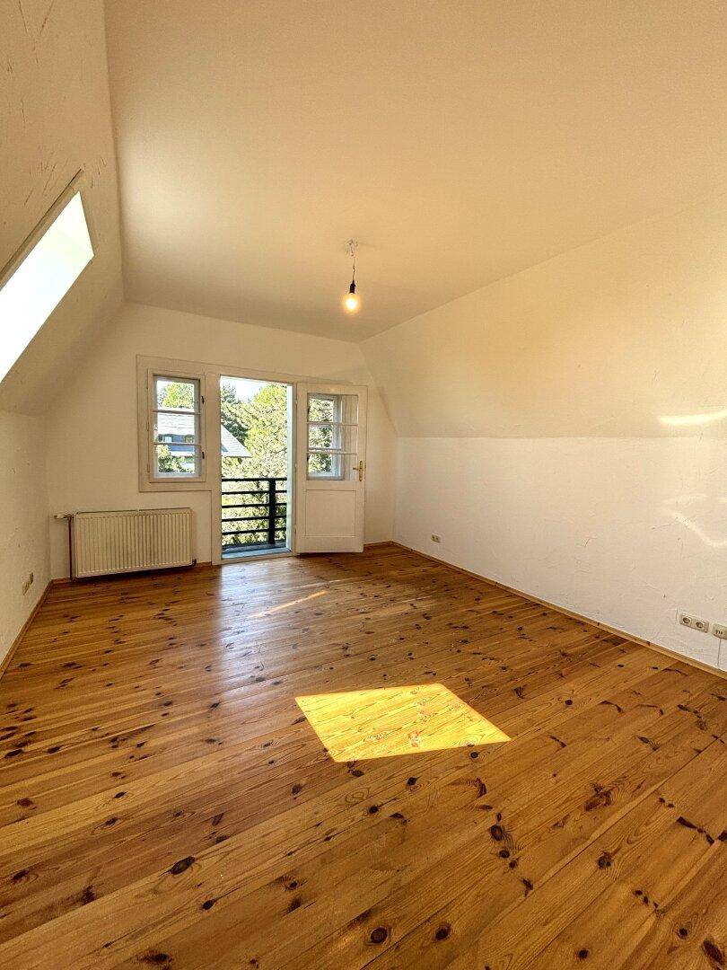 Dachgeschoss-Schlafzimmer mit Holzdielenboden, Dachfenster und Zugang zu einem französischen Balkon.
