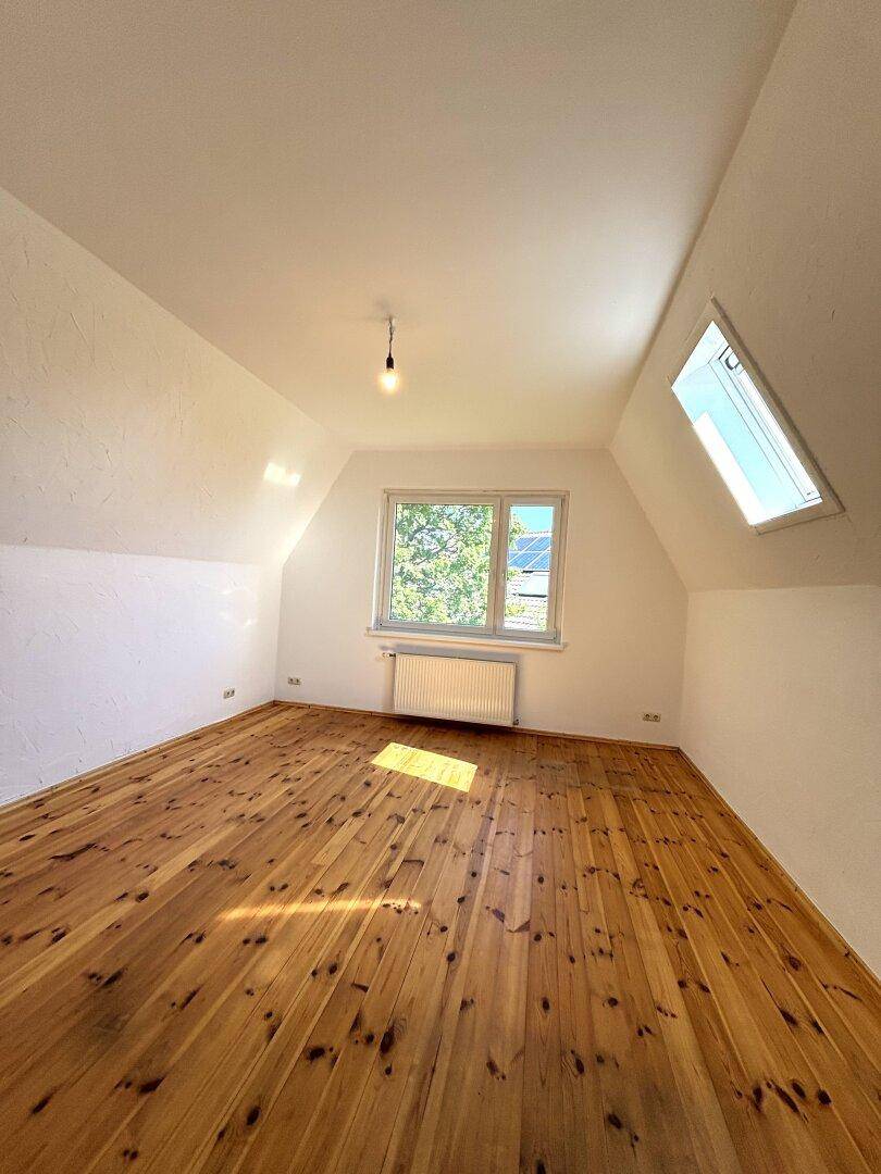 Helles Dachgeschoss-Schlafzimmer mit Holzdielenboden, Dachfenster und Blick ins Grüne.