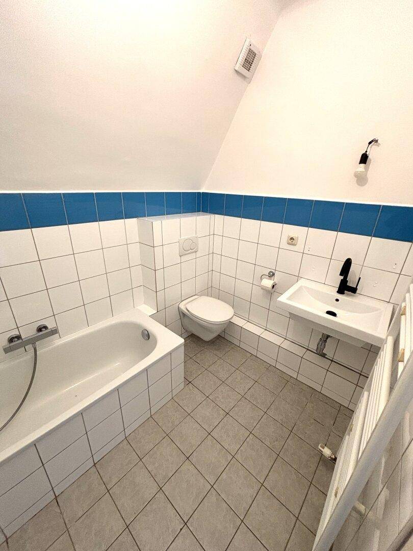 Badezimmer mit Badewanne, WC, Waschbecken und weißen Fliesen mit blauer Akzentlinie.