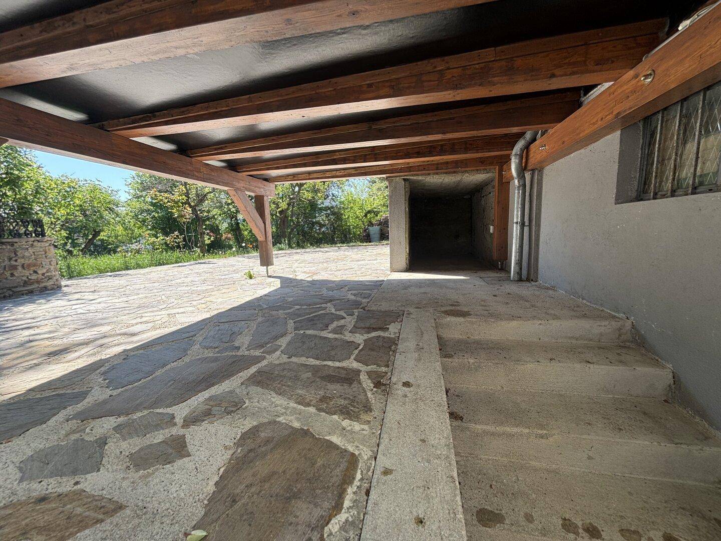 Überdachter Außenbereich mit Natursteinpflaster und Holzkonstruktion, führt zu einem Garagenzugang.