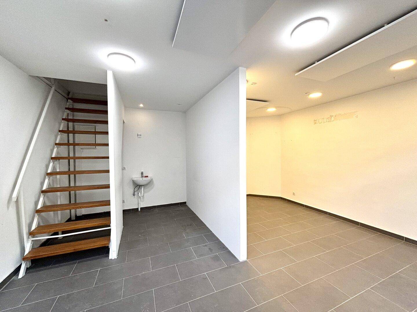 Offener Gewerberaum mit Treppe und Fliesenboden, ideal für flexible Nutzung und Kundenverkehr.
