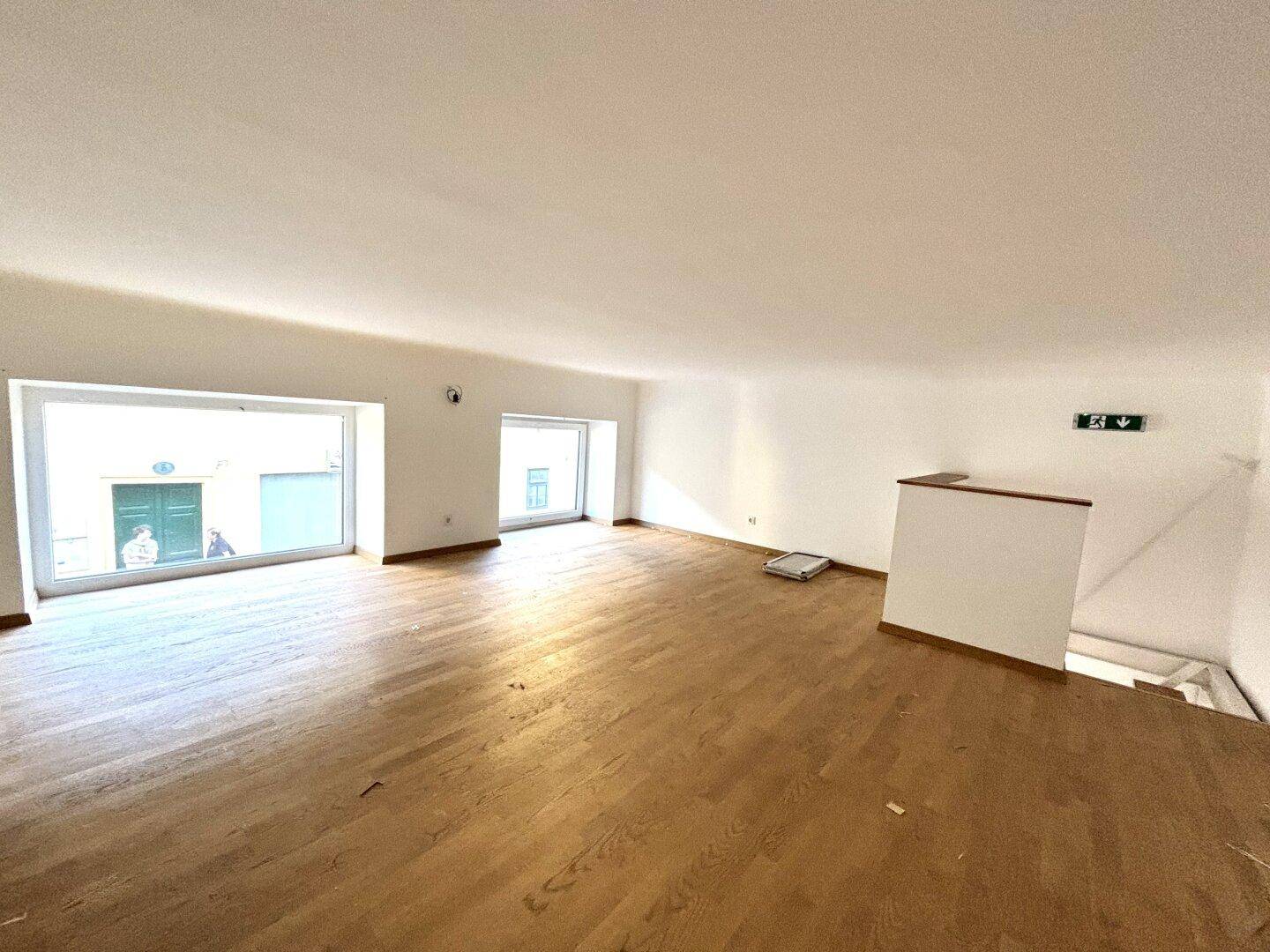 Heller und geräumiger Raum im Obergeschoss mit Holzboden und großen Fenstern, die viel Tageslicht hereinlassen.
