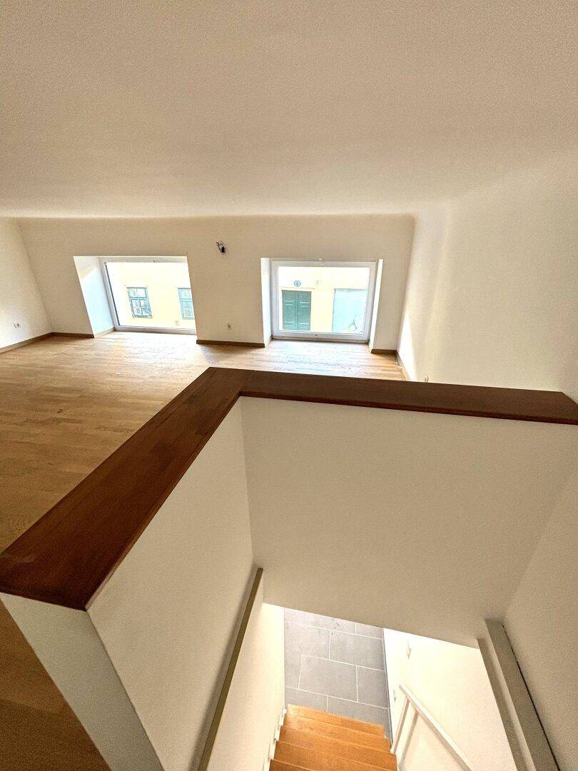 Obergeschoss mit Holzboden und zwei Dachgaubenfenstern, die einen Blick auf die Straße bieten.
