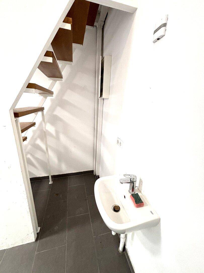 Kleines Waschbecken unter der Treppe, praktisch für Mitarbeiter oder Kunden in der Gewerbefläche.