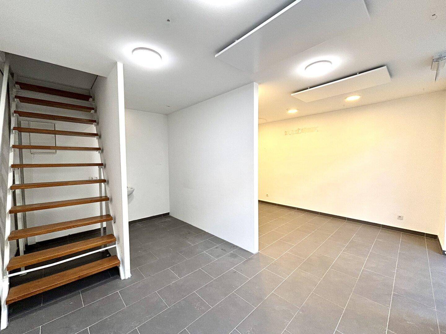 Gewerbefläche mit Treppe zum Obergeschoss und grauem Fliesenboden, bereit zur individuellen Gestaltung.