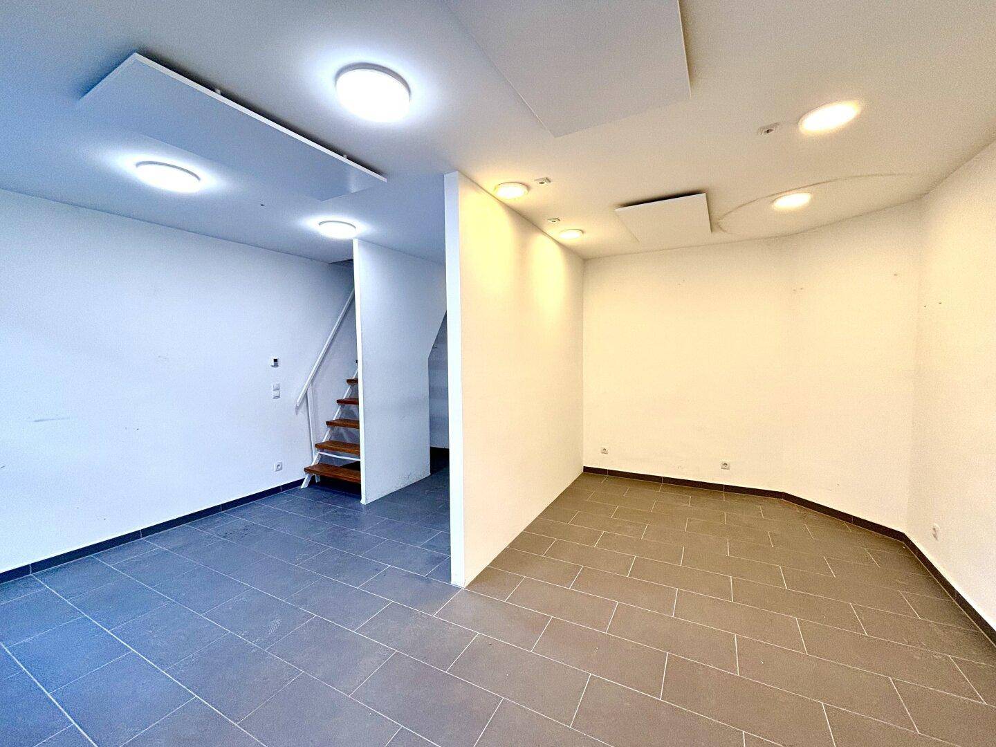 Geräumiger Ladenbereich mit offenem Grundriss, Treppe und moderner Beleuchtung, ideal für verschiedene Nutzungen.