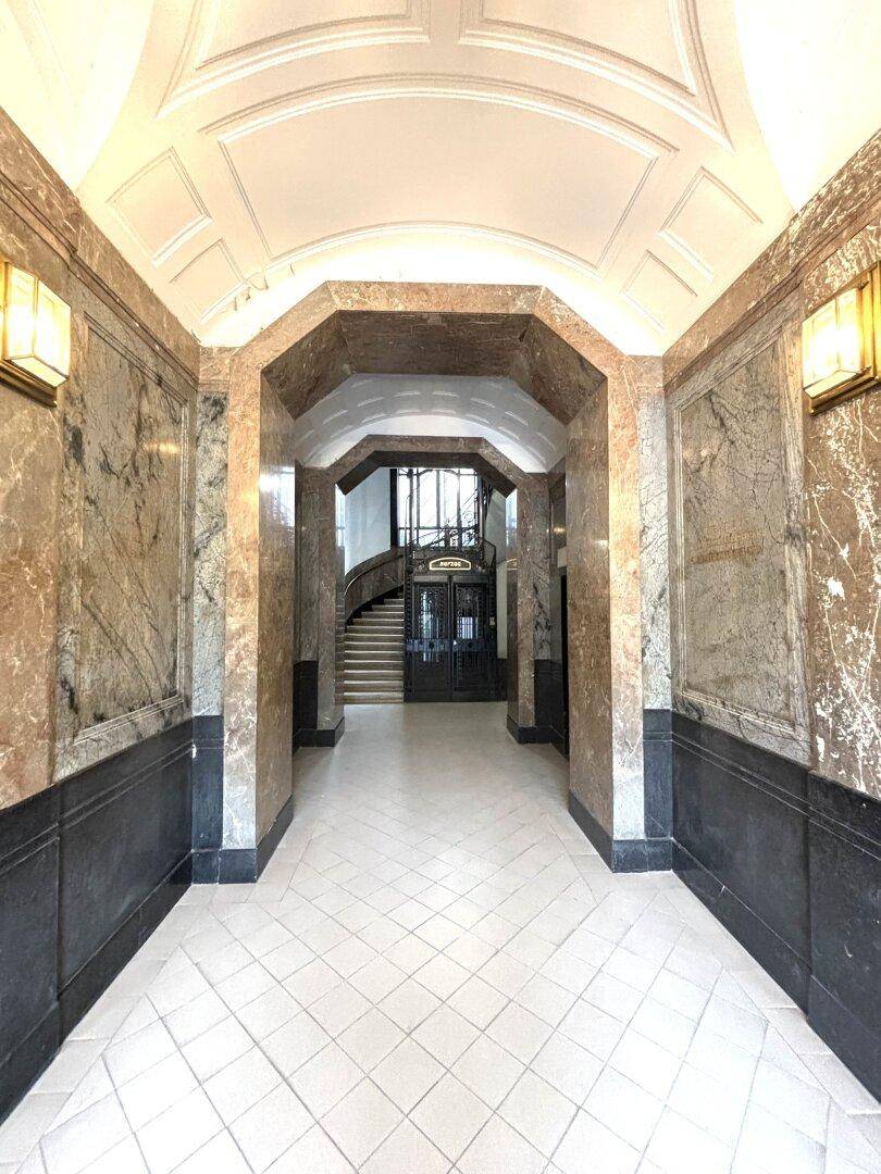 Prunkvoller Eingangsbereich mit Marmorverkleidung, hohen Decken und einem Blick auf die Treppe im Hintergrund.