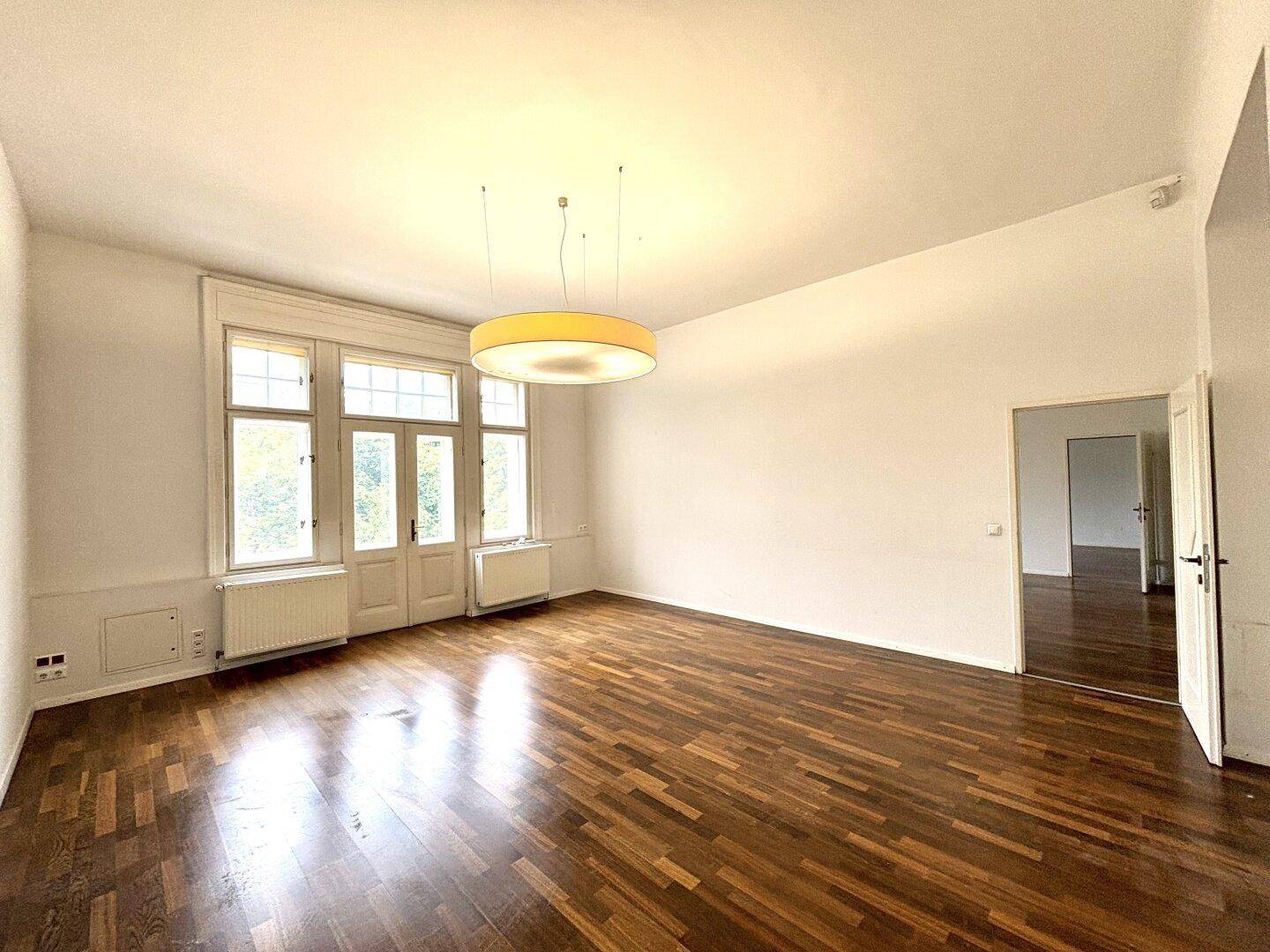 Heller, leerer Raum mit Holzboden und Zugang zu einem Balkon durch klassische Flügeltüren.