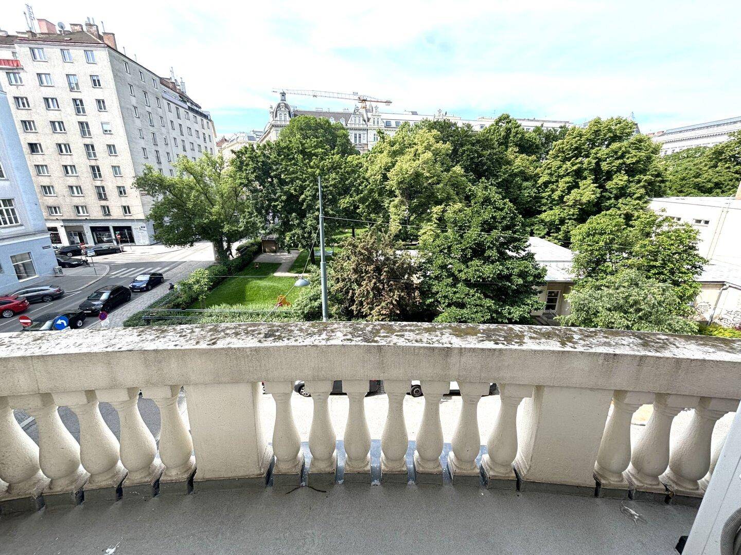 Balkon mit klassischem Balustradengeländer und Blick auf eine grüne Parkanlage und die umliegende Stadt.