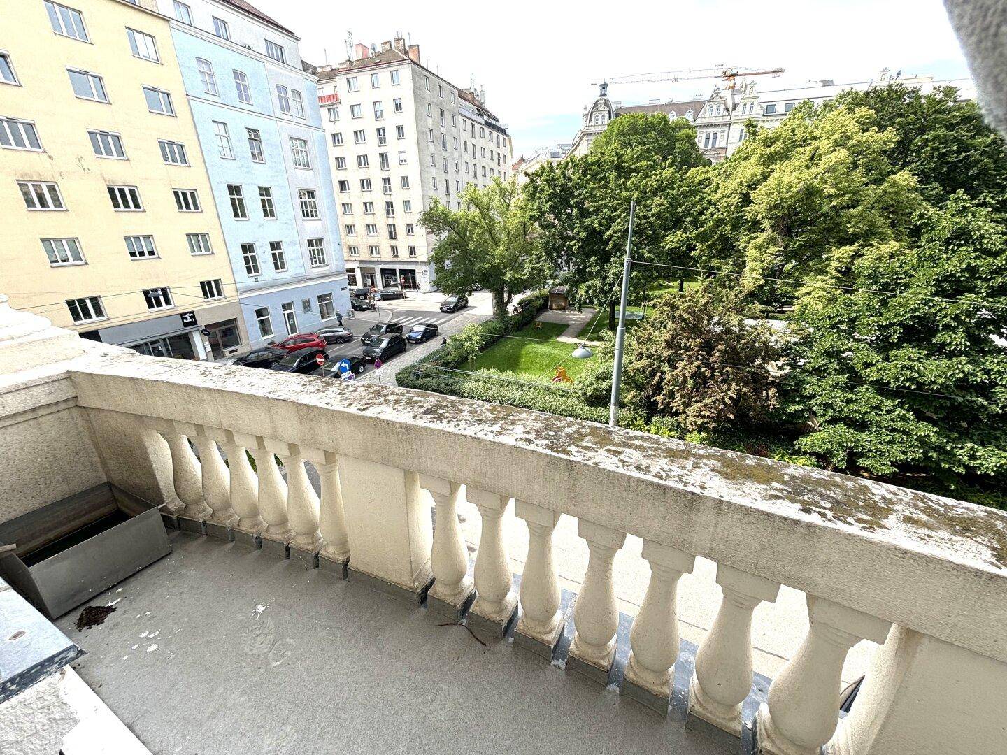 Balkon mit klassischem Balustradengeländer und Blick auf eine grüne Parkanlage und die umliegende Stadt.