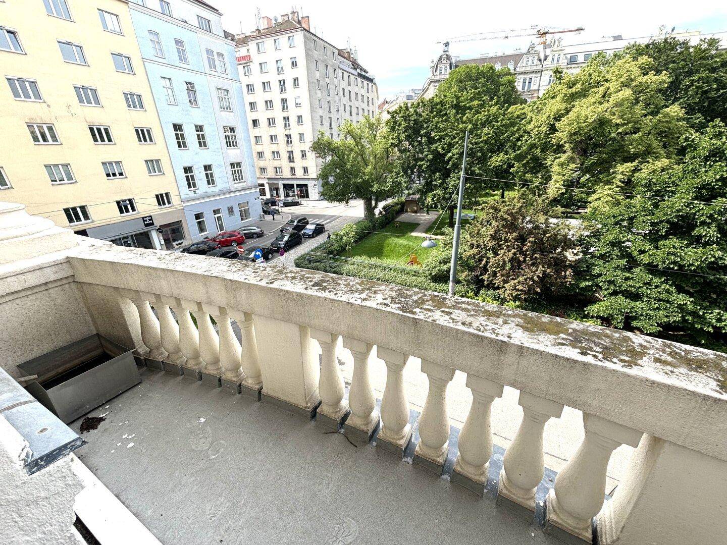 Balkon mit klassischem Balustradengeländer und Blick auf eine grüne Parkanlage und die umliegende Stadt.