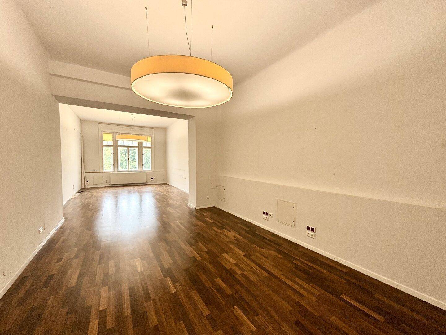 Großer, heller Raum mit Holzboden und einem Fensterbereich, der viel Tageslicht bietet.