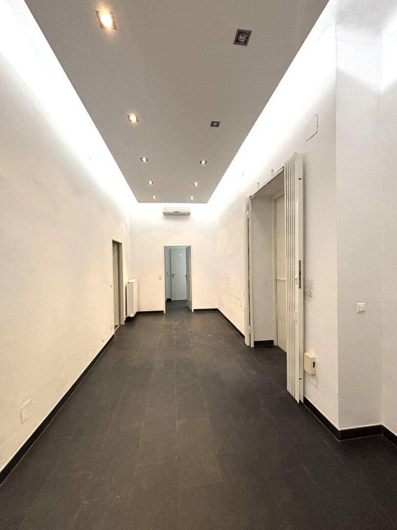 Langer, leerer Flur mit dunklen Fliesen und integrierter Deckenbeleuchtung, der zu weiteren Räumen führt.