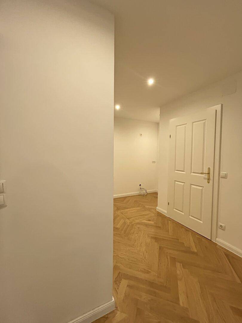 Langer Flur mit Fischgrätparkett und einer weißen Tür, der einen Übergang zu anderen Bereichen schafft.