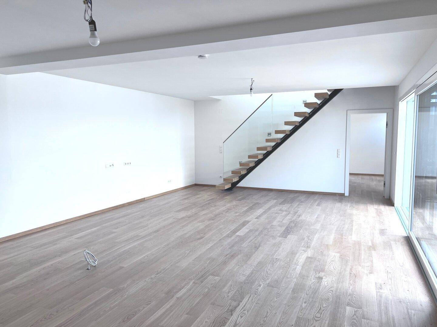 Heller, leerer Wohnbereich mit Holzboden und moderner Treppe, bereit zur individuellen Gestaltung.