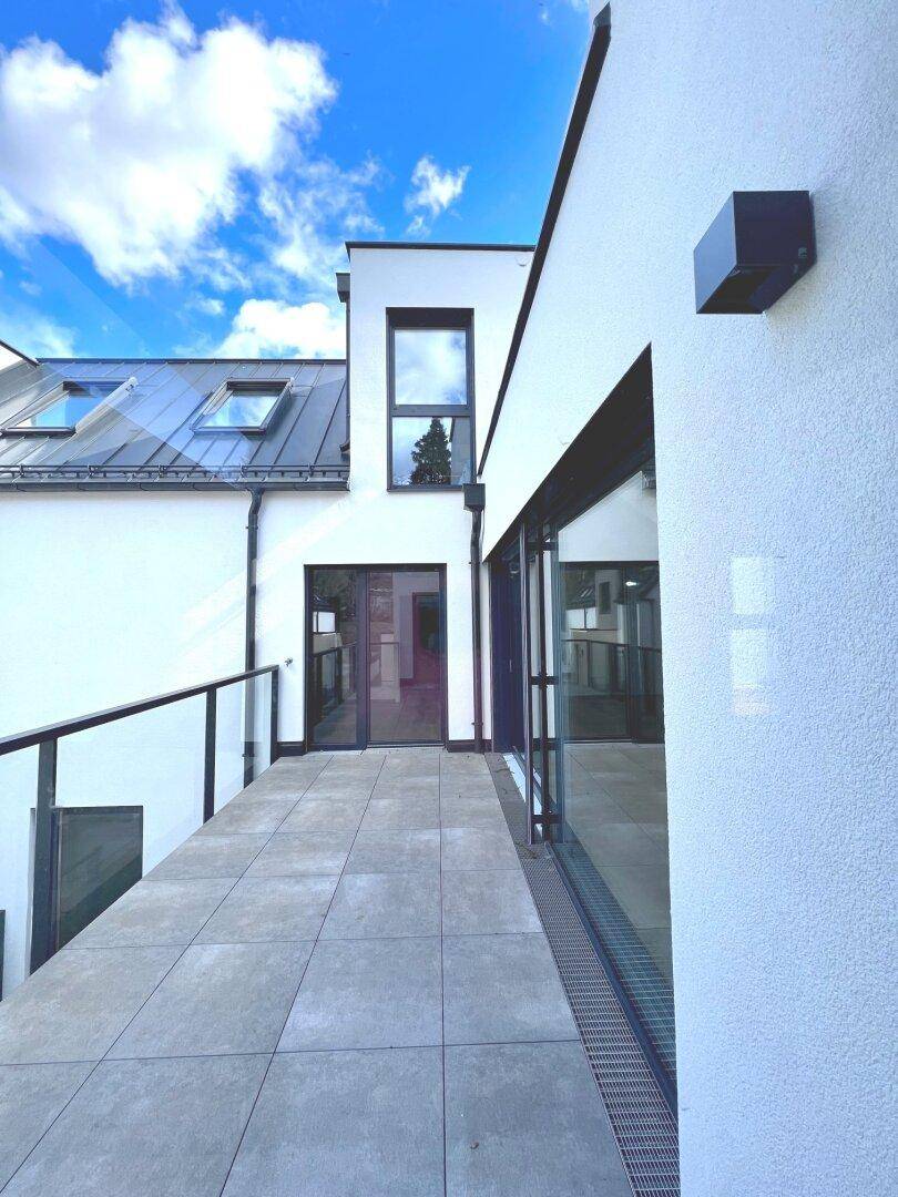 Schmale Außenterrasse mit Fliesenboden und moderner Fassade, ideal für entspannte Stunden.
