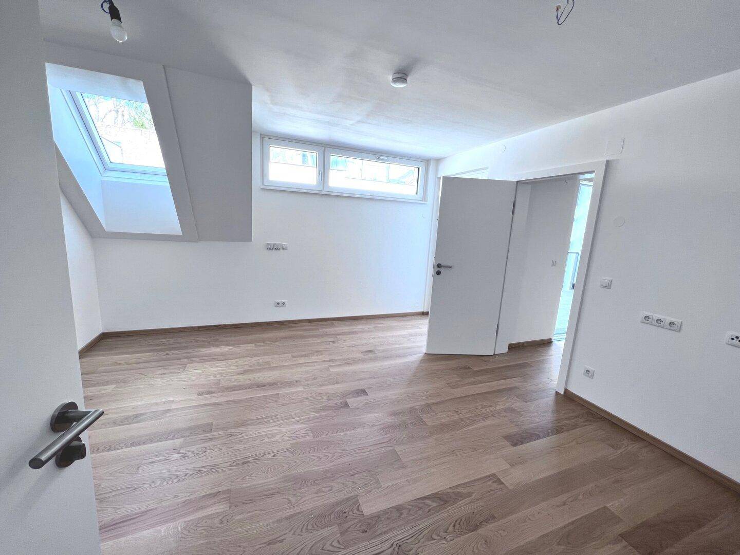 Leeres Schlafzimmer im Dachgeschoss mit Holzboden, Dachfenster und viel Tageslicht.