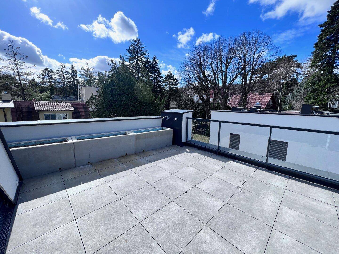 Weitläufige Dachterrasse mit modernen Fliesen und Glasgeländer unter strahlend blauem Himmel.