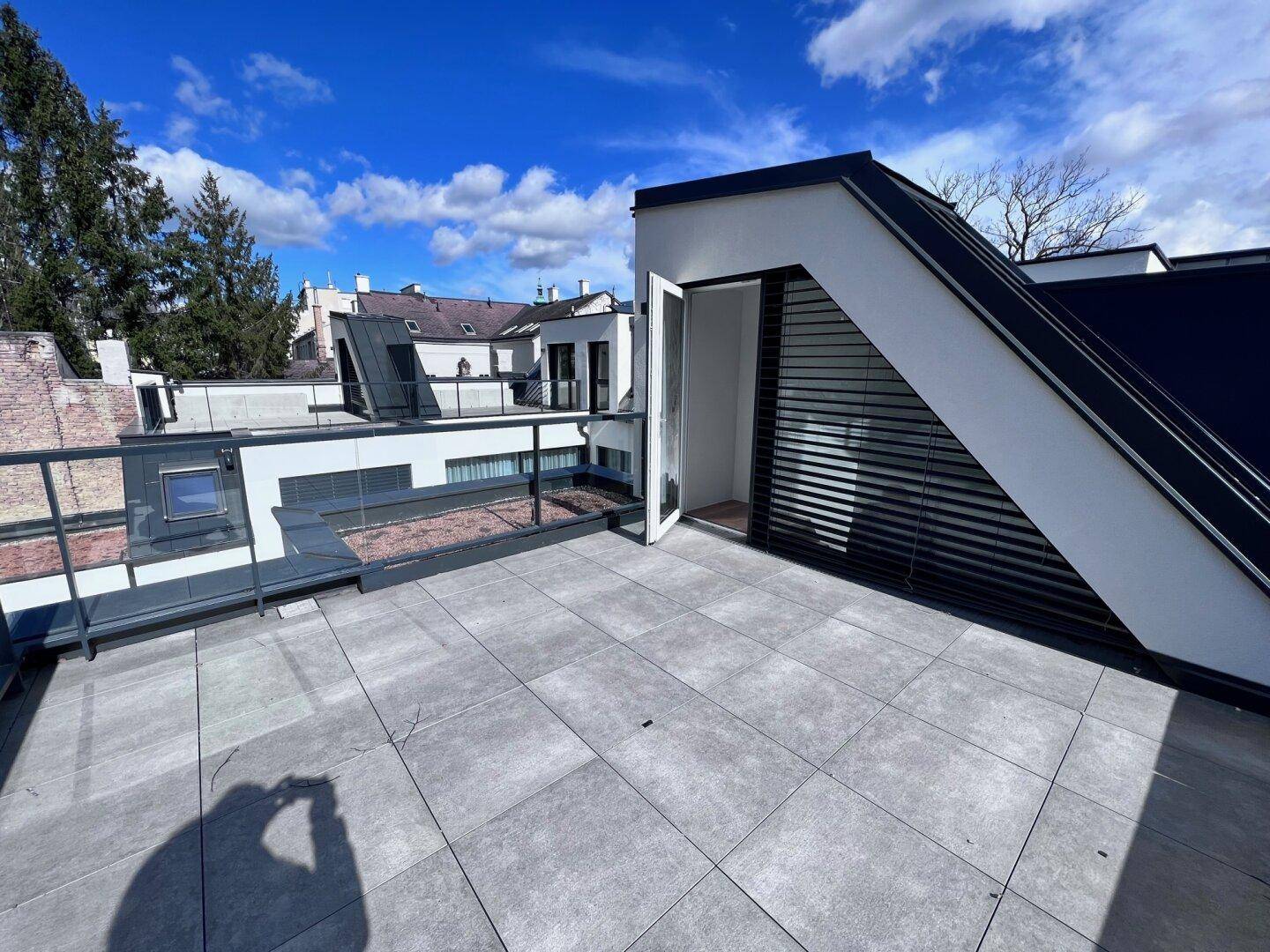 Dachterrasse mit Fliesenboden und moderner Architektur, umgeben von weiteren Gebäuden.