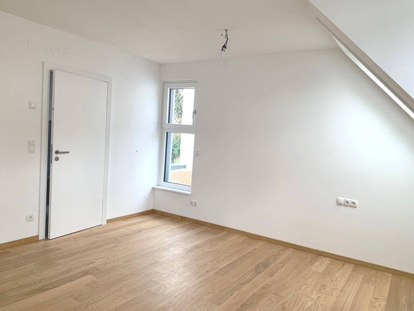 Helles, leeres Schlafzimmer mit Holzboden und Fenster, bereit zur individuellen Einrichtung.
