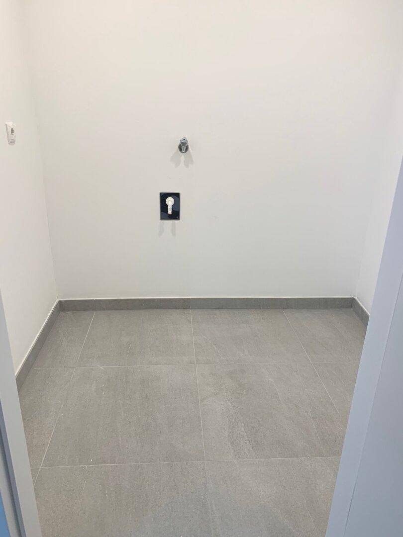 Leerer Hauswirtschaftsraum mit Fliesenboden und Anschlüssen für Waschmaschine und Trockner.