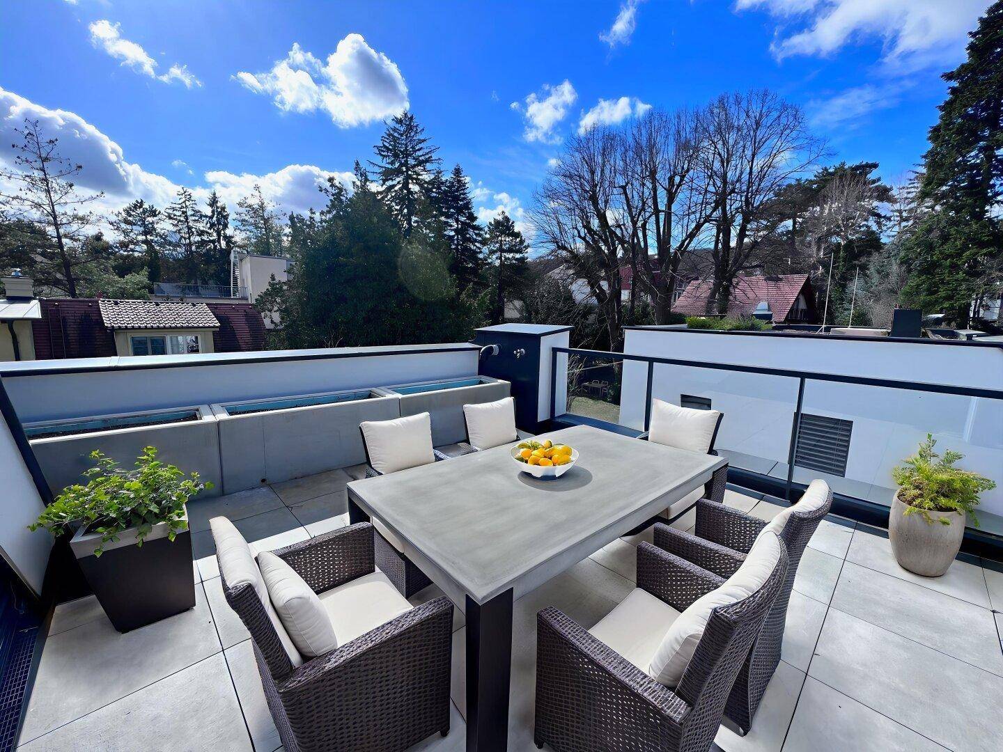 Geräumige Dachterrasse mit modernen Gartenmöbeln und weitem Blick ins Grüne unter blauem Himmel.