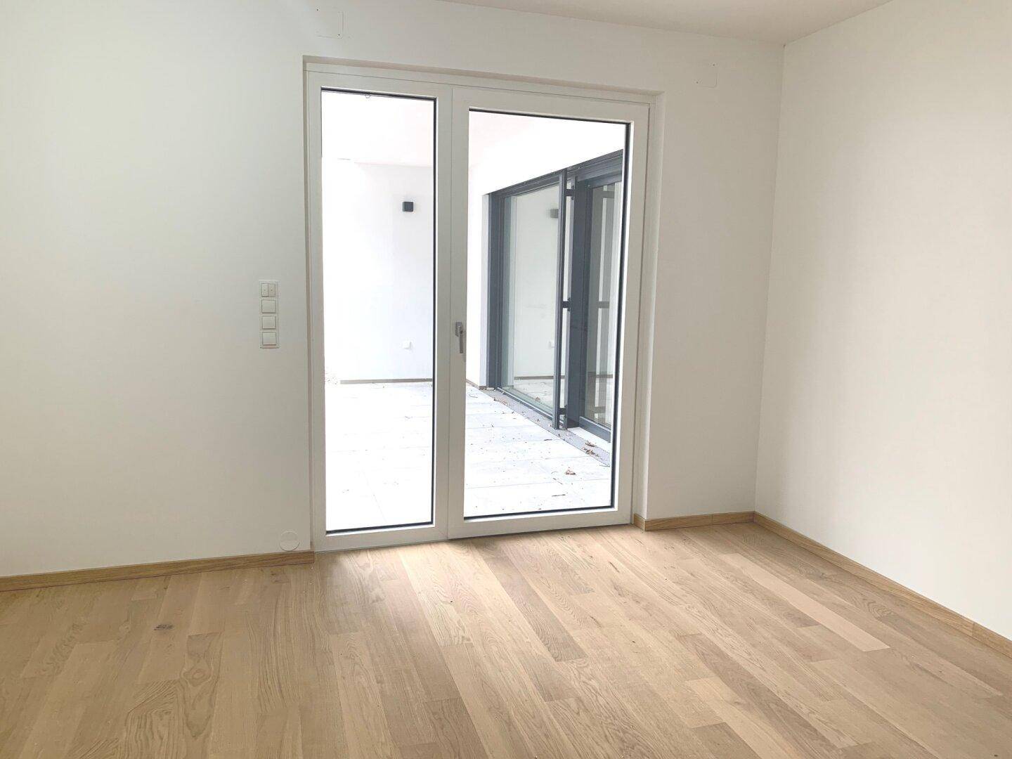 Leeres Zimmer mit Holzboden und großen Fenstern, ideal als Schlaf- oder Arbeitszimmer.