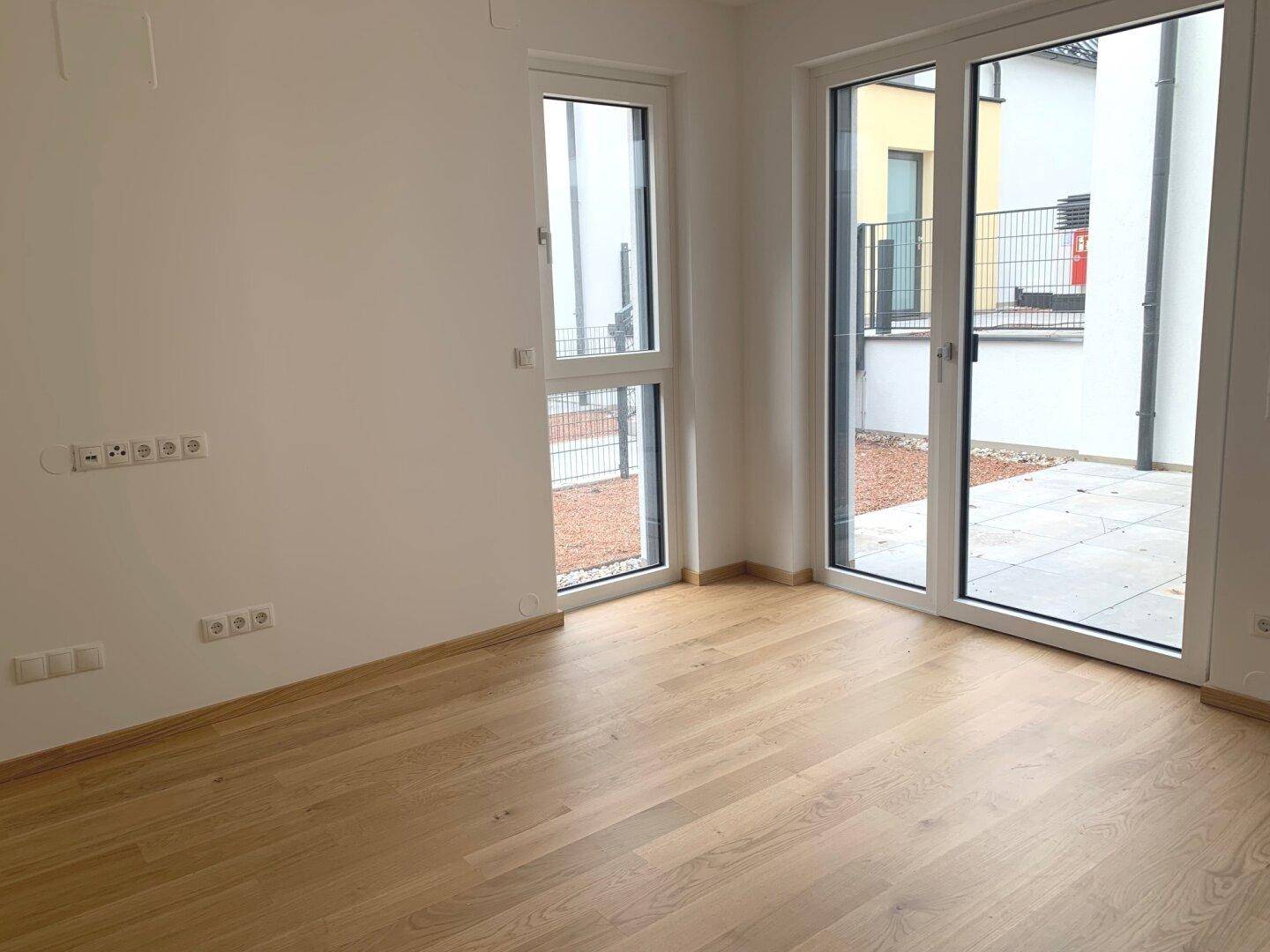 Leeres Zimmer mit Holzboden und großen Fenstern, ideal als Schlaf- oder Arbeitszimmer.