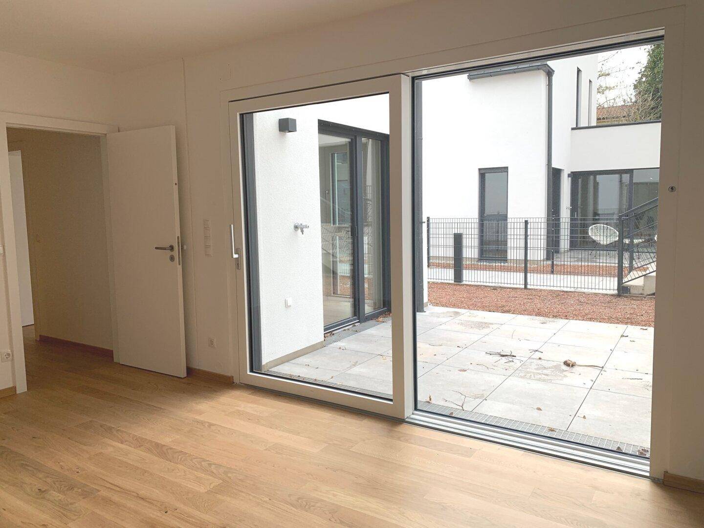 Leeres Zimmer mit Holzboden und großen Schiebetüren zu einem Außenbereich.