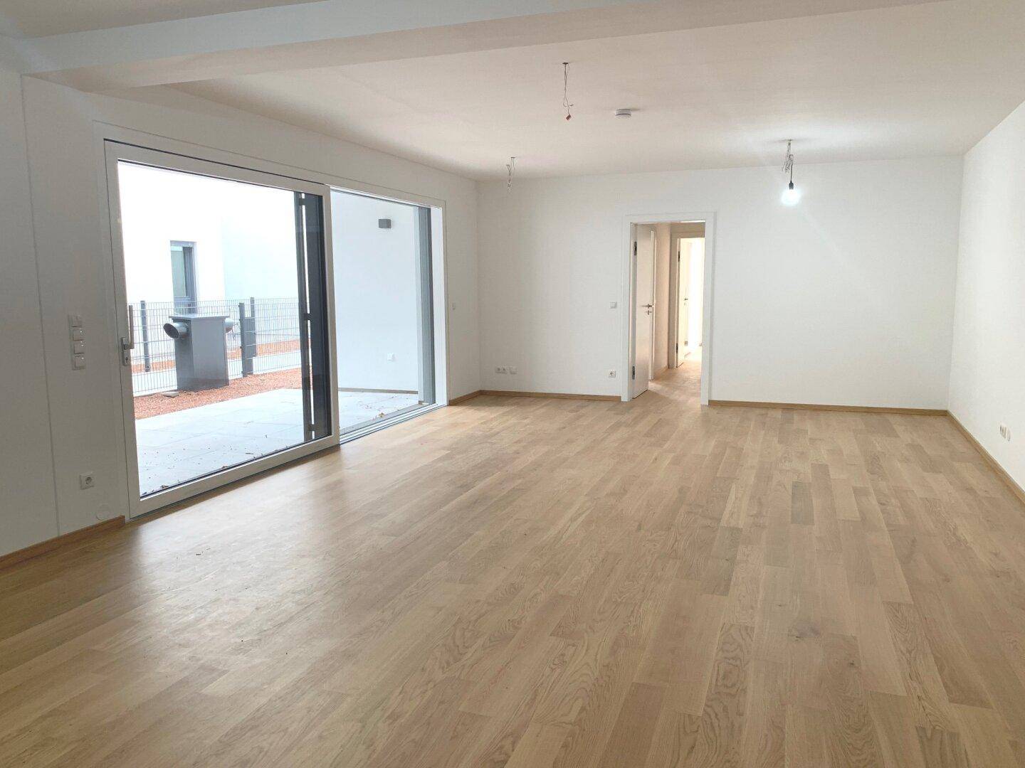 Heller, leerer Wohnbereich mit Holzboden und großen Schiebetüren zu einem Außenbereich.