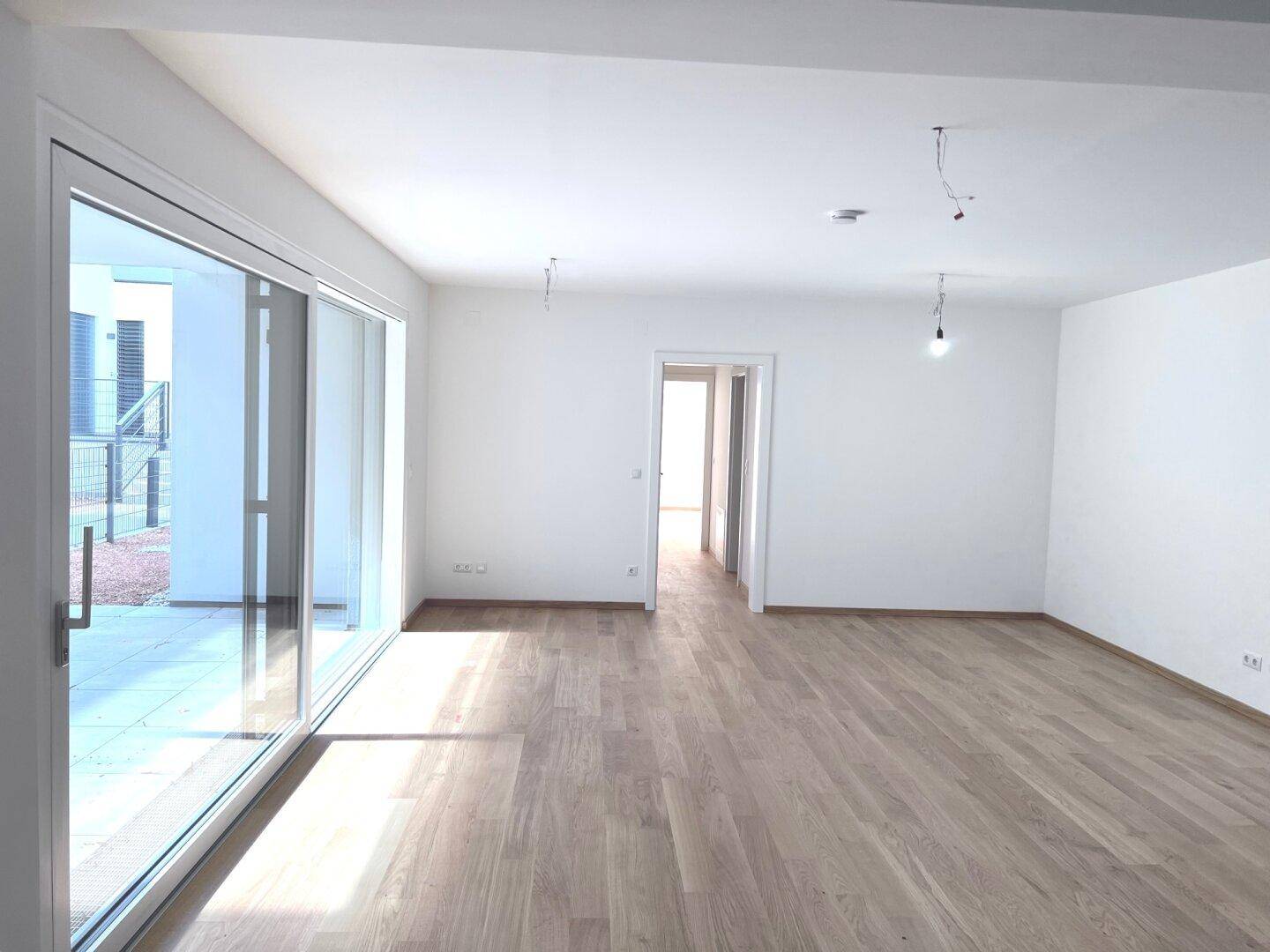 Heller, leerer Wohnbereich mit Holzboden und großen Schiebetüren zum Außenbereich.