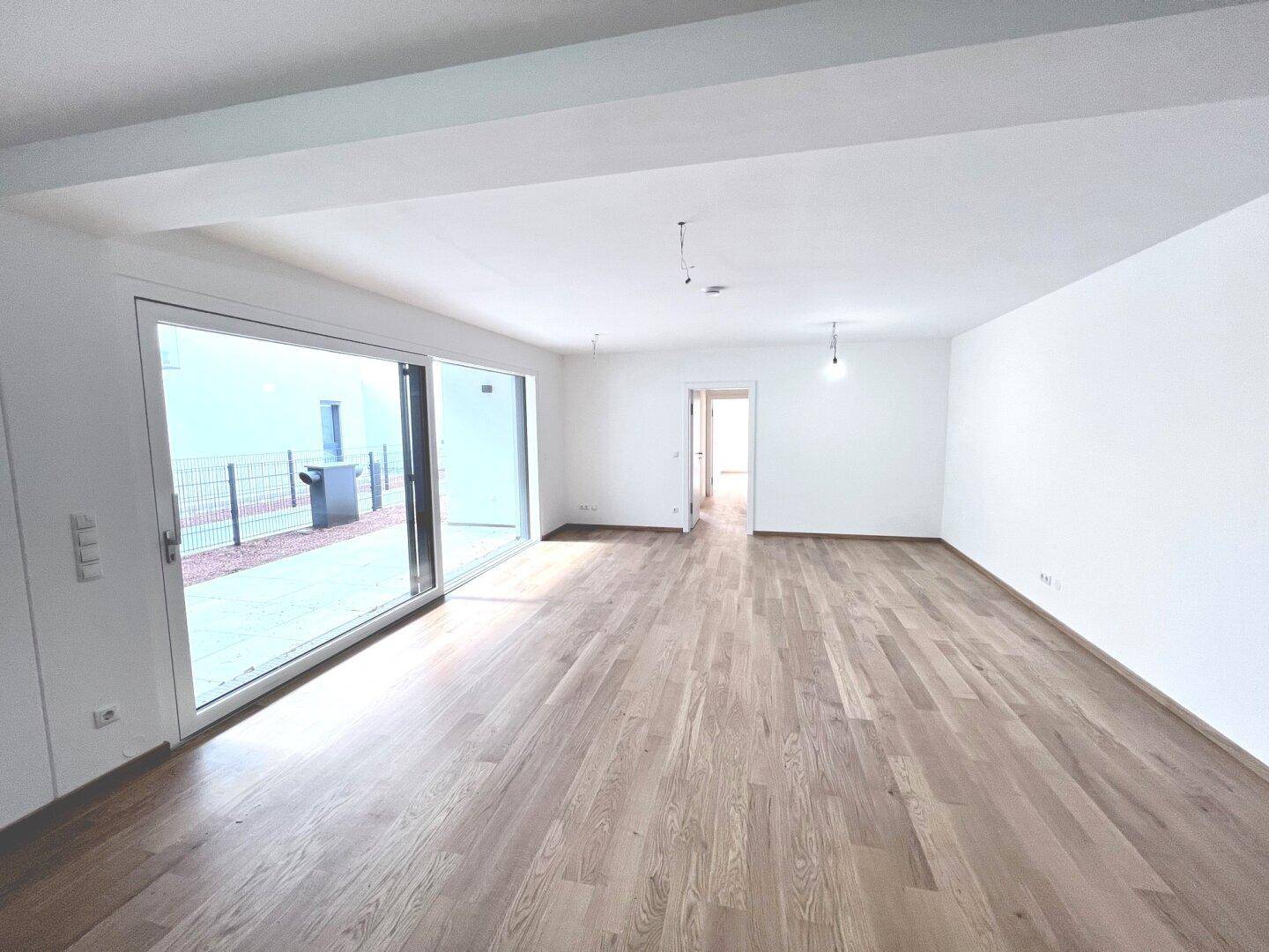 Großer, leerer Wohnbereich mit Holzboden und breiten Schiebetüren zum Außenbereich.