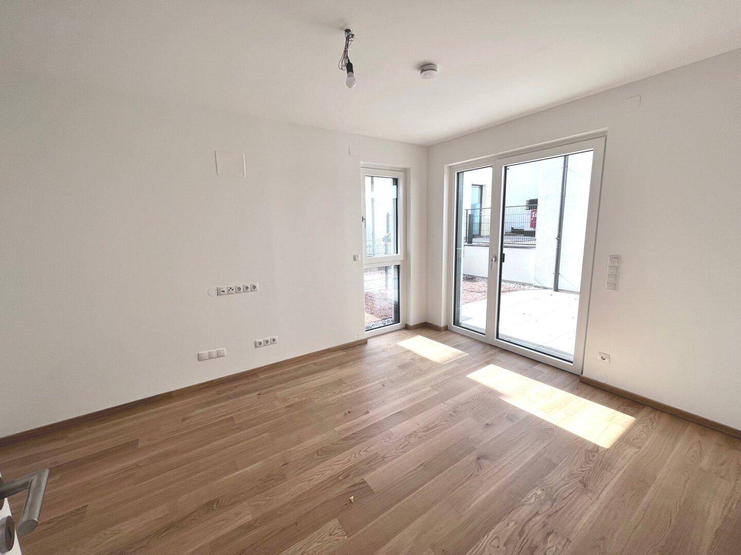 Leeres Zimmer mit Holzboden und großen Fenstern, ideal als Schlaf- oder Arbeitszimmer.