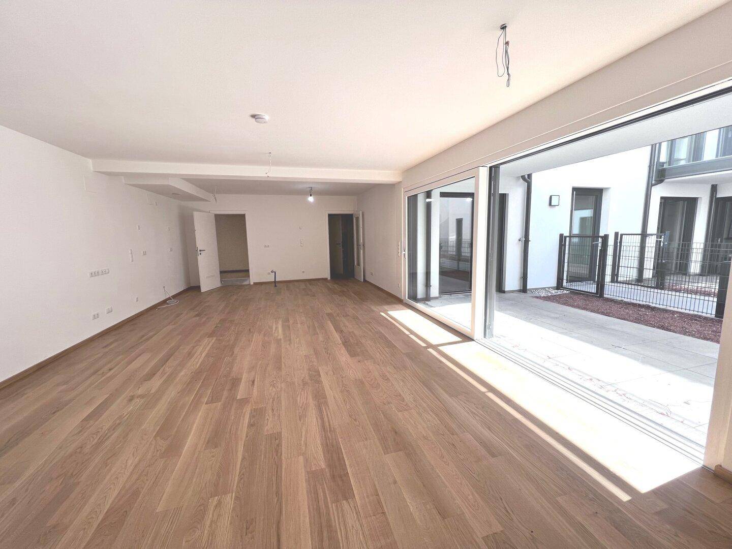 Geräumiger, leerer Wohnbereich mit Holzboden und großen Schiebetüren zum Außenbereich.