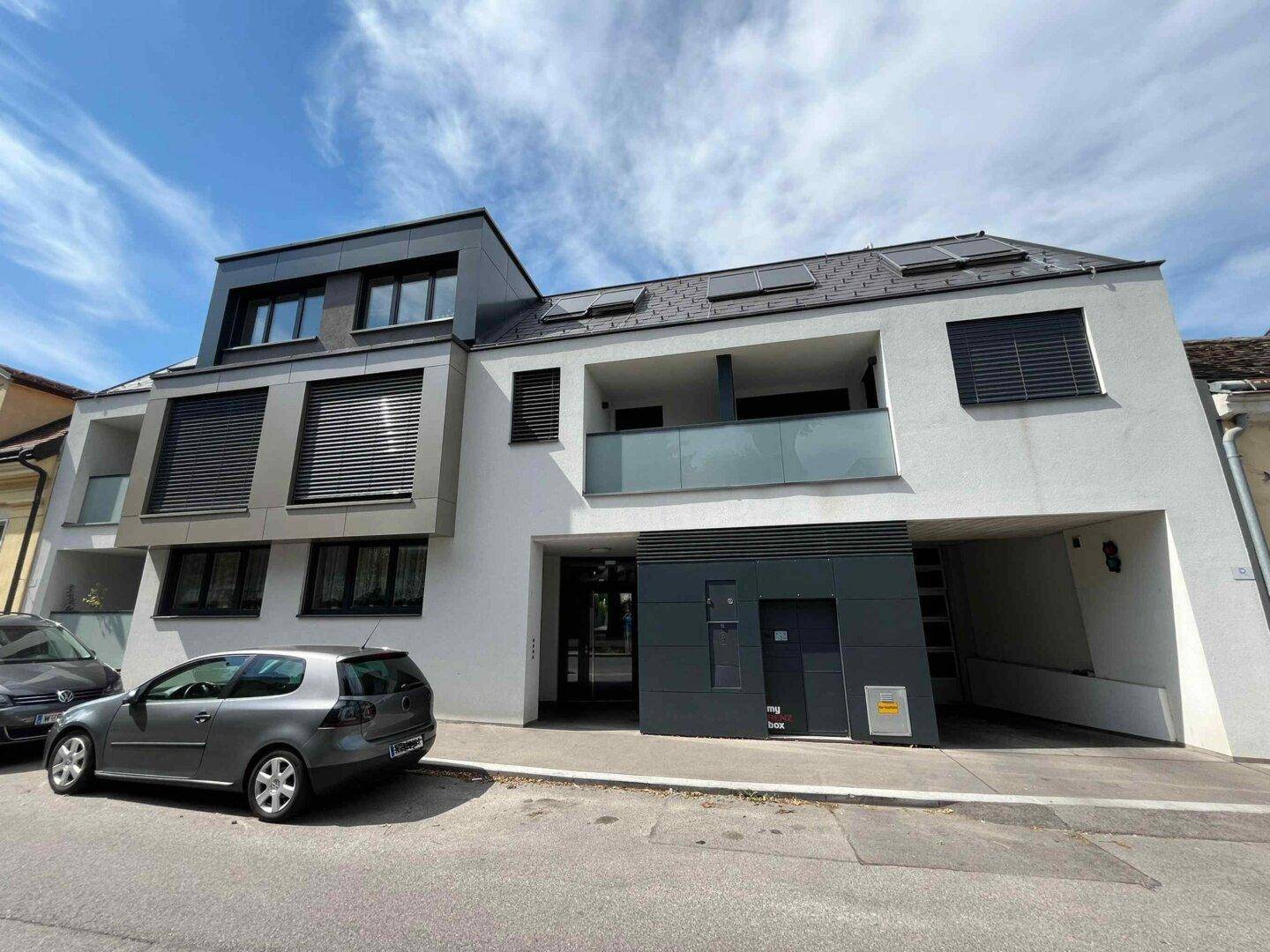 Moderne Wohnanlage mit weißer Fassade, Balkonen und großen Fenstern unter blauem Himmel.