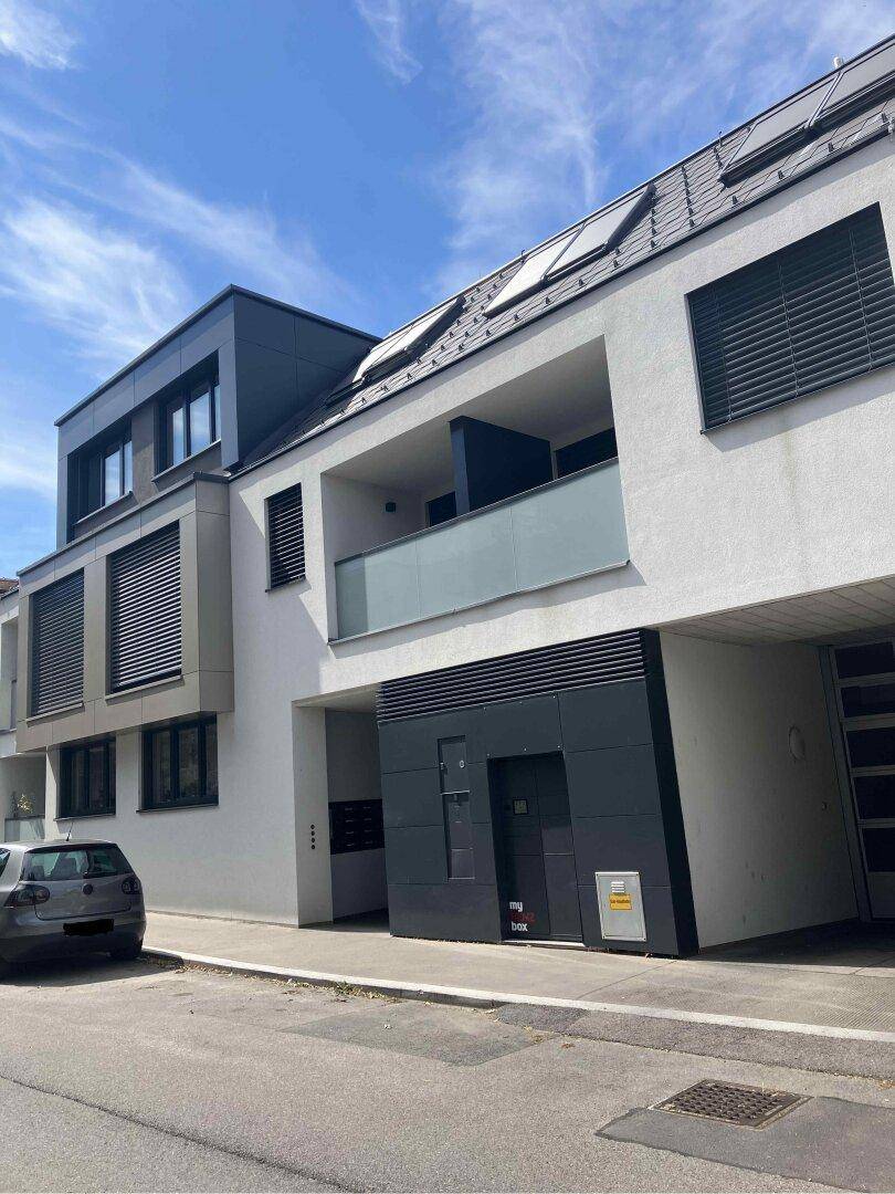 Moderne Wohnanlage mit weißer Fassade, dunklen Akzenten und Parkmöglichkeiten an der Straße.
