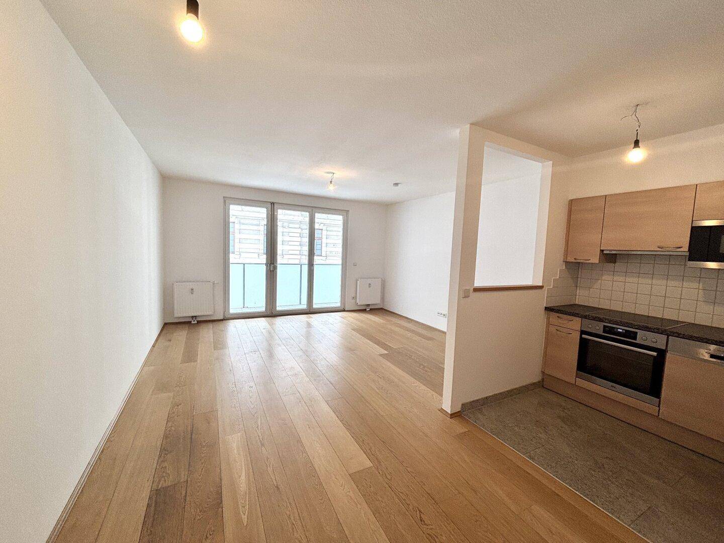 Leerer Wohn-Essbereich mit Holzboden und Zugang zum Balkon.